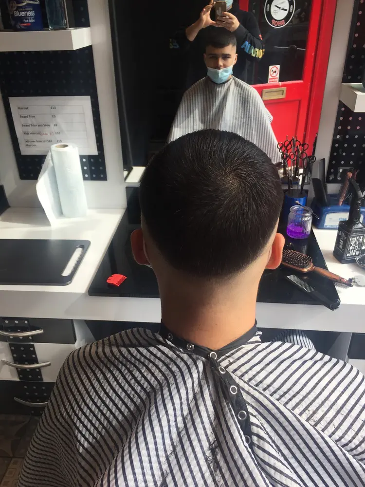 Skin fade in progress at Pasa Barbers, the printed price list on the pegboard behind