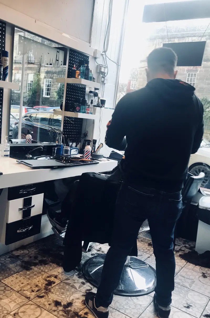 The barber standing at the window of Pasa Barbers between customers, looking out onto Raeburn Place